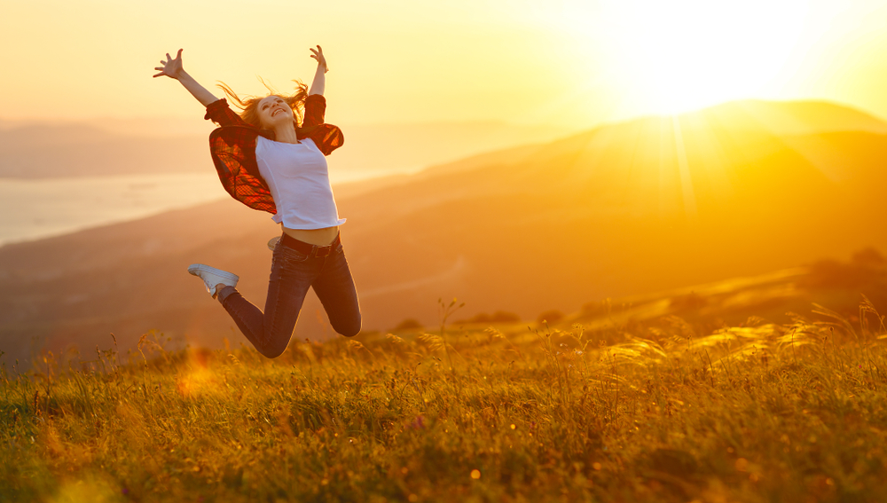 Person joyfully jumping in a field at sunset.