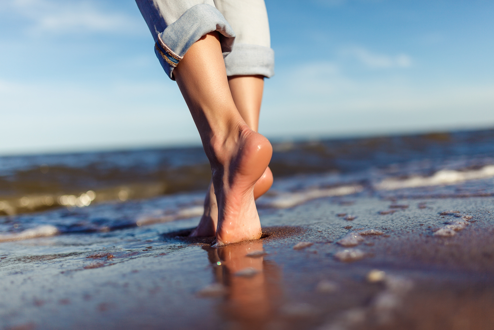 Bare feet walking along wet sand by the ocean, representing healthy foot mobility and podiatry care.